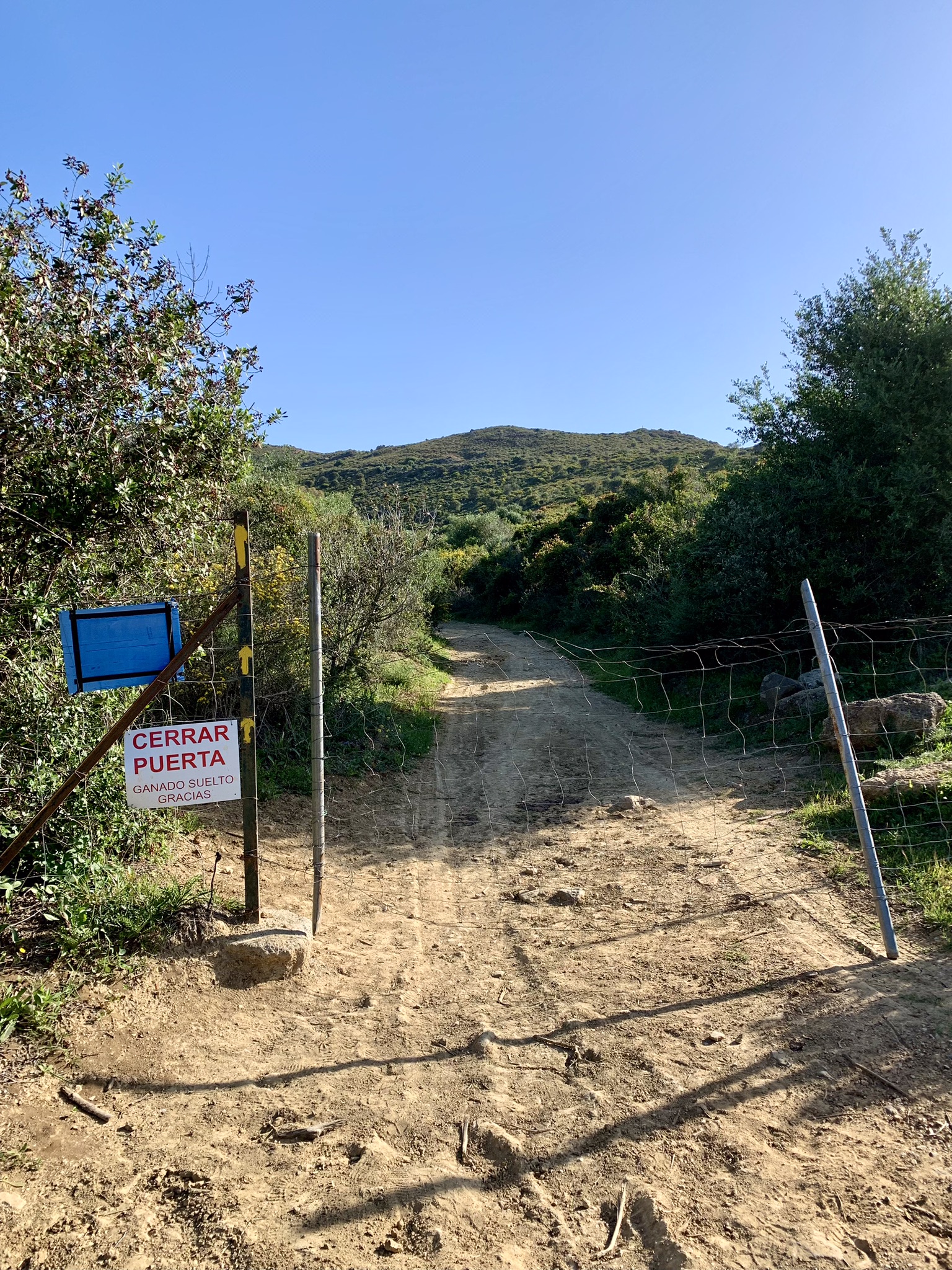 A wire fence across the path on the Via Serrana with yellow arrows painted on the gate post